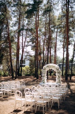 Beyaz narin sandalyeleri ve yumuşak çigila kemeri olan bir çam ormanında güzel bir düğün sahnesi. Doğal ortam huzurlu ve romantik bir atmosfer yaratır.