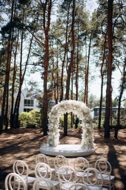 Beyaz narin sandalyeleri ve yumuşak çigila kemeri olan bir çam ormanında güzel bir düğün sahnesi. Doğal ortam huzurlu ve romantik bir atmosfer yaratır.