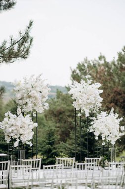 Göl kenarında beyazlarla süslenmiş lüks bir açık hava düğün töreni. Zarif bir çiçek kemeri, şeffaf sandalyeler, yeşil bir çimen ve fevkalade bir arka plan.