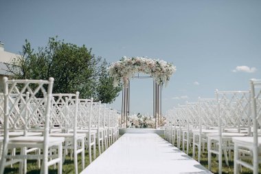 Lüks bir düğün sahnesi, beyaz bir patika boyunca dizilmiş beyaz dantel sandalyeli yüksek çiçekli bir kemer.