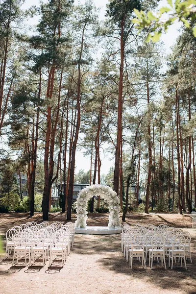 Beyaz narin sandalyeleri ve yumuşak çigila kemeri olan bir çam ormanında güzel bir düğün sahnesi. Doğal ortam huzurlu ve romantik bir atmosfer yaratır.
