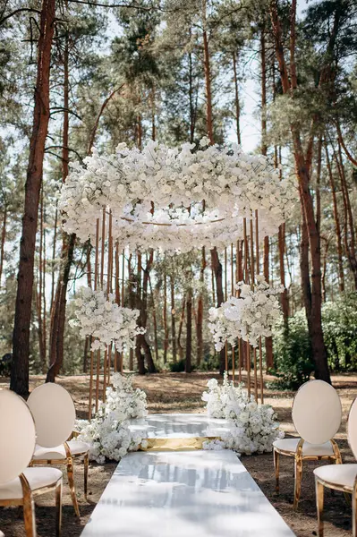 Bir çam ormanında gösterişli bir düğün, beyaz ayaklı zarif beyaz sandalyeler, beyaz çiçeklerle süslenmiş uzun bir kemer ve el değmemiş beyaz bir koridor.