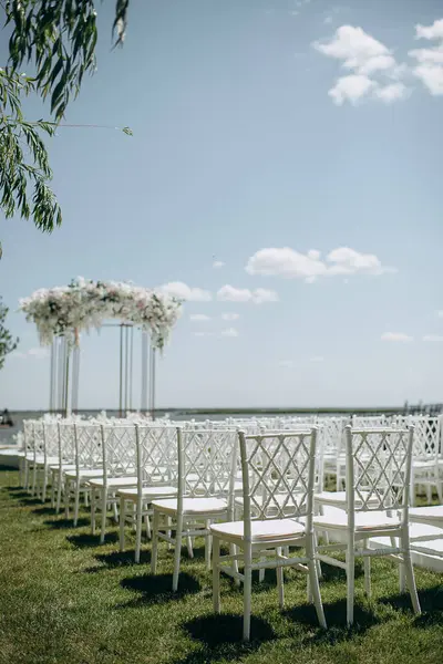 Lüks bir düğün sahnesi, beyaz bir patika boyunca dizilmiş beyaz dantel sandalyeli yüksek çiçekli bir kemer.