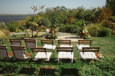 Yeşillik ve renkli çiçeklerden yapılmış küçük bir arka bahçe çayırı, katlanır ahşap sandalyelerle birlikte, büyüleyici bir açık hava düğünü yaratıyor.