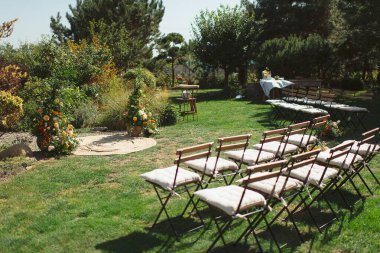 Yeşillik ve renkli çiçeklerden yapılmış küçük bir arka bahçe çayırı, katlanır ahşap sandalyelerle birlikte, büyüleyici bir açık hava düğünü yaratıyor.