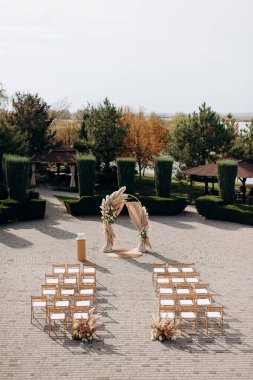 Uçsuz bucaksız bir avluda büyük bir tören. Etrafı budanmış çalılar ve ağaçlarla çevrili.