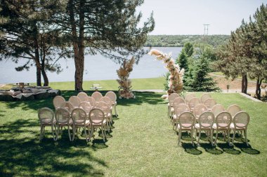 Dokuma sandalyeler ve çimen kemerleriyle donatılmış şık bir açık hava düğün töreni.