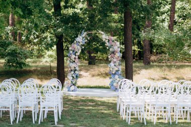 Çiçekli düğün kemeri, yeşil ormanda beyaz sandalyeler.