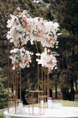 Çiçekli düğün kemeri, beyaz ve pembe çiçeklerle ve cam mum tutacaklarıyla bir ormanda