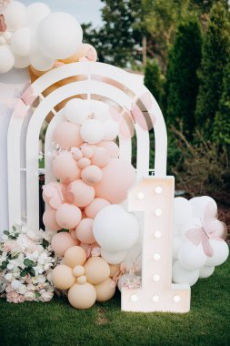 Açık hava doğum günü fotoğraf bölgesi, beyaz kemer, pembe balonlar ve neon doğum günü tabelası.
