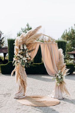 Çimlerle süslenmiş bir düğün kemeri ve taş bir verandada duran kumaş.