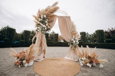 Çimlerle süslenmiş bir düğün kemeri ve taş bir verandada duran kumaş.