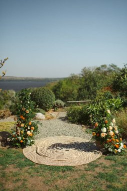 Dairesel bir jüt halı, açık havada çiçeklerle süslenmiş manzaralı bir manzaraya yol açar.