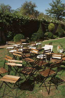 Ahşap katlanır sandalyeler yeşil bir çimenlikte dizilmiş ve bahçesinde iplik lambaları var.