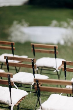 Bej yastıklı ahşap katlanır sandalyeler açık havada yeşil bir çimenlikte duruyor.