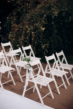 Çiçek buketleriyle süslenmiş beyaz ahşap sandalyeler açık havada bir taş terasta dizilmiş.