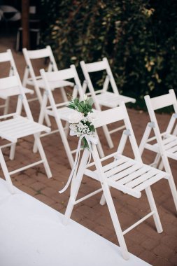 Çiçek buketleriyle süslenmiş beyaz ahşap sandalyeler açık havada bir taş terasta dizilmiş.