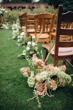 Ahşap sandalyeler açık havada çiçek aranjmanlarıyla süslenmiş yeşil bir çimenlik.