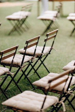 Bej yastıklı ahşap katlanır sandalyeler açık havada yeşil bir çimenlikte duruyor.