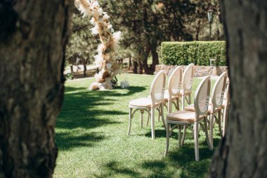 Yuvarlak dokuma sandalyeler, arka planda bir göl bulunan yeşil çimenlikteki çiçek kemerine bakıyor.