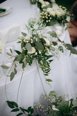 Beyaz bir çiçek süsü, okaliptüs ve beyaz bir masa örtüsü üzerinde bebek nefesi.