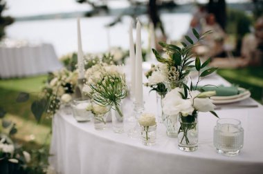 Açık hava etkinliğinde beyaz masa örtüsü üzerinde mumlar olan beyaz bir çiçek süsü.