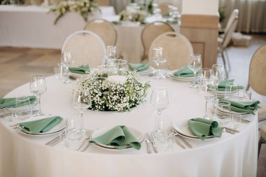 Bir etkinlik ortamında zarif cam eşyalar ve çiçekli yuvarlak masa seti.