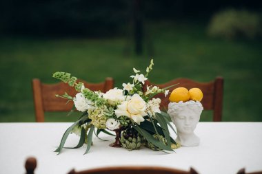 Beyaz güller ve beyaz bir masa örtüsünün üstündeki vazoda limonlar olan zarif bir masa.