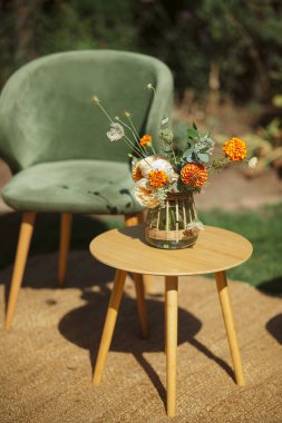 Portakal ve beyaz çiçek buketi örülmüş vazoda, küçük ahşap bir masada.