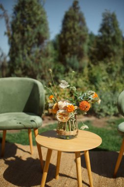 Portakal ve beyaz çiçek buketi örülmüş vazoda, küçük ahşap bir masada.