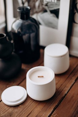 Ahşap bir masanın üzerinde beyaz alçı kavanozlarında birkaç mum, tahta filizler, siyah cam vazolar ve bir tablo bulunan estetik bir kompozisyon. Şık ve rahat bir iç dekorasyon düzeneği