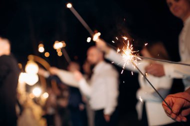 Geceleri yanan bir maytap tutan bir elin yakın çekimi.