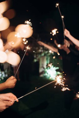 Geceleri yanan bir maytap tutan bir elin yakın çekimi.