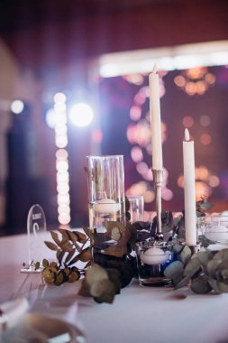 Lokantadaki bir ziyafet masasında yanan ince, beyaz mumların içinde bir çok ince beyaz mum var. Kutlama ya da ziyafet için pastel tonlar ve şık, minimalist bir atmosfer var.