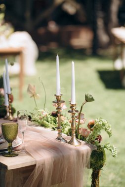 Mumlarla süslenmiş bir açık hava ziyafet masası ve nilüfer ve yosun gibi eşsiz yeşil bitkilerden oluşan bir kompozisyon kutlama için egzotik ve zarif bir atmosfer yaratıyor.
