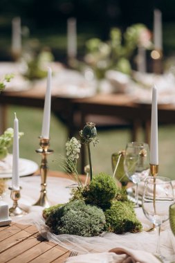 Mumlarla süslenmiş bir açık hava ziyafet masası ve nilüfer ve yosun gibi eşsiz yeşil bitkilerden oluşan bir kompozisyon kutlama için egzotik ve zarif bir atmosfer yaratıyor.