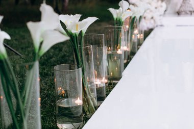 Cam kürelerde süzülen mumlar ve zarif beyaz çiçekler düğün kemerine giden beyaz yolu süsler romantik ve sofistike bir atmosfer yaratır.