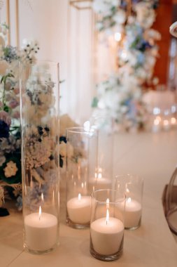 Bir çok sütun mum çiçek desenli düğün kemerinin dibinde cam kürelerde yanıyor, kutlama için romantik ve zarif bir atmosfer yaratıyor.