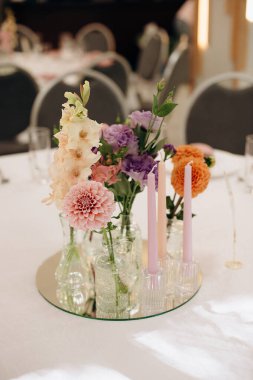 Restorandaki ziyafet masasının dekorunda uzun mumlar ve canlı sonbahar çiçekleri kutlama için sıcak ve şenlikli bir atmosfer yaratıyor.