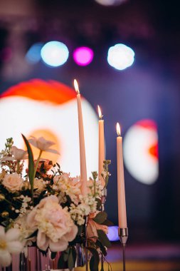 Restorandaki ziyafet masasının dekorunda uzun mumlar ve canlı sonbahar çiçekleri kutlama için sıcak ve şenlikli bir atmosfer yaratıyor.