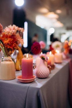 Yeni evlilerin başkanlığı için sonbahar temalı dekor, vazolarda canlı çiçekler, yanan mumlar ve pembe ve lavanta tonlarında masa örtüleri, romantik ve zarif bir atmosfer yaratıyor.