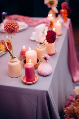 Yeni evlilerin başkanlığı için sonbahar temalı dekor, vazolarda canlı çiçekler, yanan mumlar ve pembe ve lavanta tonlarında masa örtüleri, romantik ve zarif bir atmosfer yaratıyor.