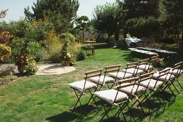 Yeşillik ve renkli çiçeklerden yapılmış küçük bir arka bahçe çayırı, katlanır ahşap sandalyelerle birlikte, büyüleyici bir açık hava düğünü yaratıyor.
