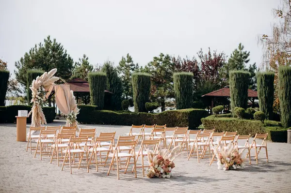 Uçsuz bucaksız bir avluda büyük bir tören. Etrafı budanmış çalılar ve ağaçlarla çevrili.