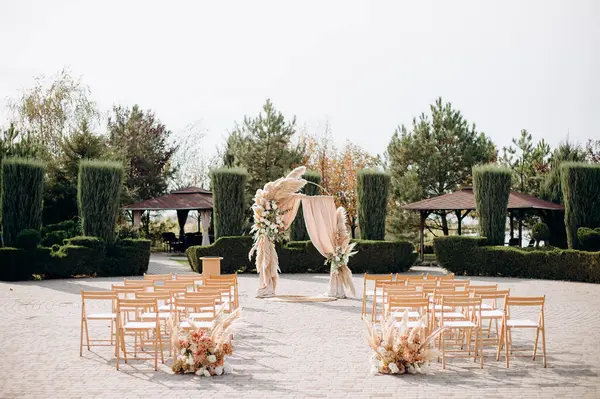 Uçsuz bucaksız bir avluda büyük bir tören. Etrafı budanmış çalılar ve ağaçlarla çevrili.