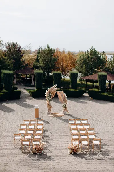 Uçsuz bucaksız bir avluda büyük bir tören. Etrafı budanmış çalılar ve ağaçlarla çevrili.