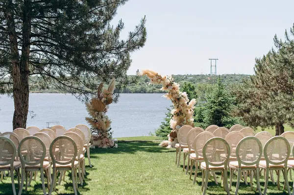 Dokuma sandalyeler ve çimen kemerleriyle donatılmış şık bir açık hava düğün töreni.
