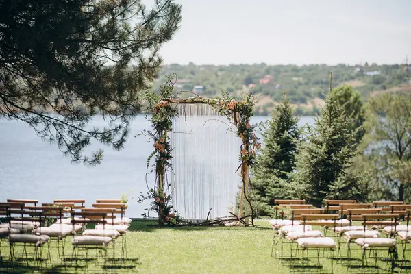 Açık havada, kemerli ve göle bakan ahşap sandalyeli bir düğün.