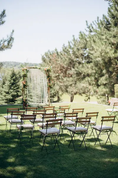 Açık havada, kemerli ve göle bakan ahşap sandalyeli bir düğün.