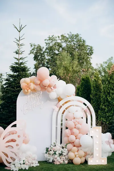 Açık hava doğum günü fotoğraf bölgesi, beyaz kemer, pembe balonlar ve neon doğum günü tabelası.
